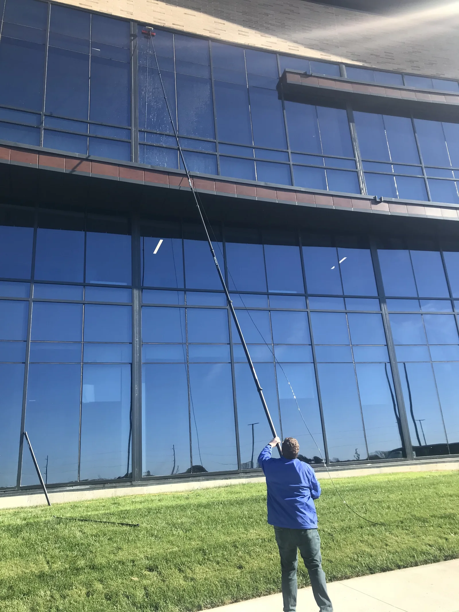 S.S. Window Cleaning technician using a water-fed pole on a multi-storey glass office facade