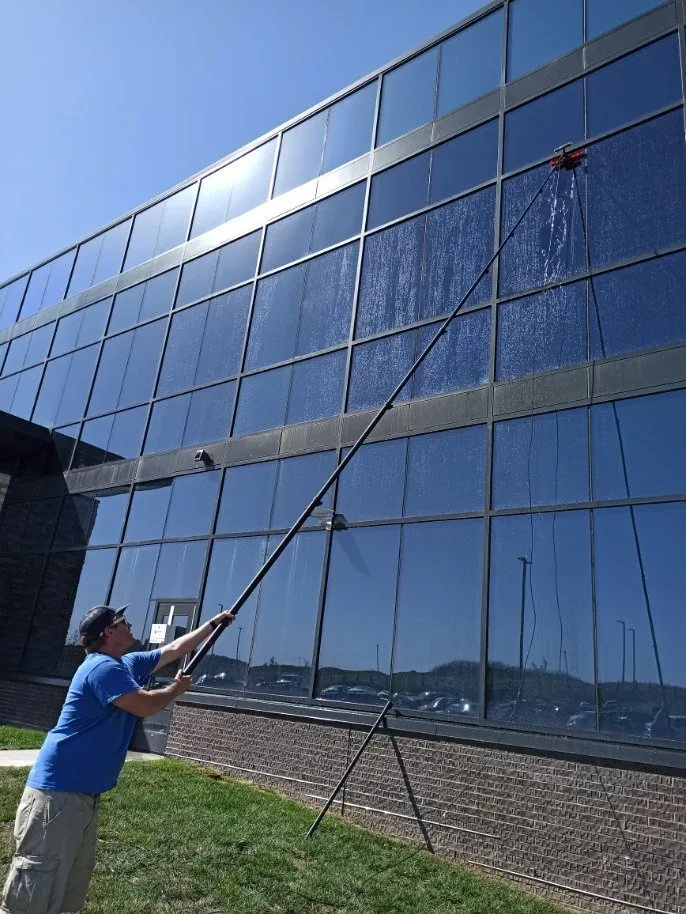 Crew member reaching upper-storey windows on a commercial building with an extension pole