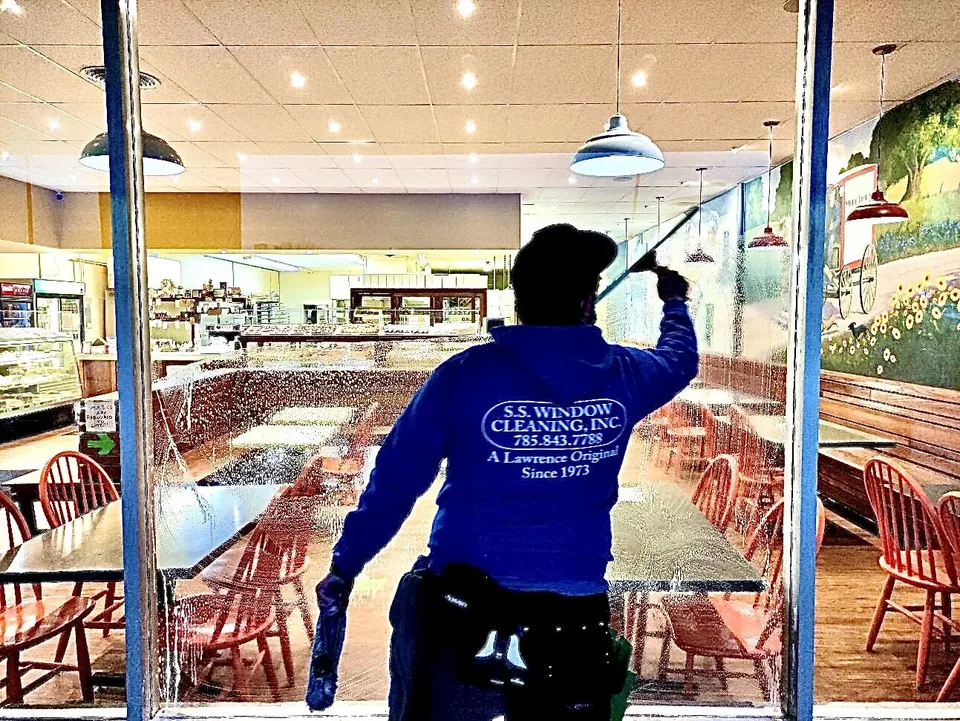 S.S. Window Cleaning crew member in a branded hoodie cleaning a bakery storefront window