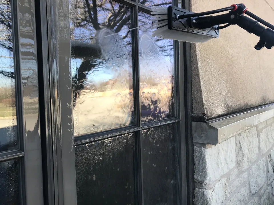 Water-fed brush rinsing a divided-light residential window on a stone house