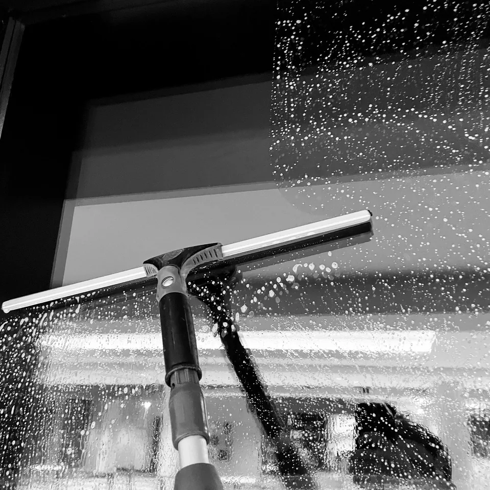 Close-up of a squeegee pulling water down a soapy pane of glass